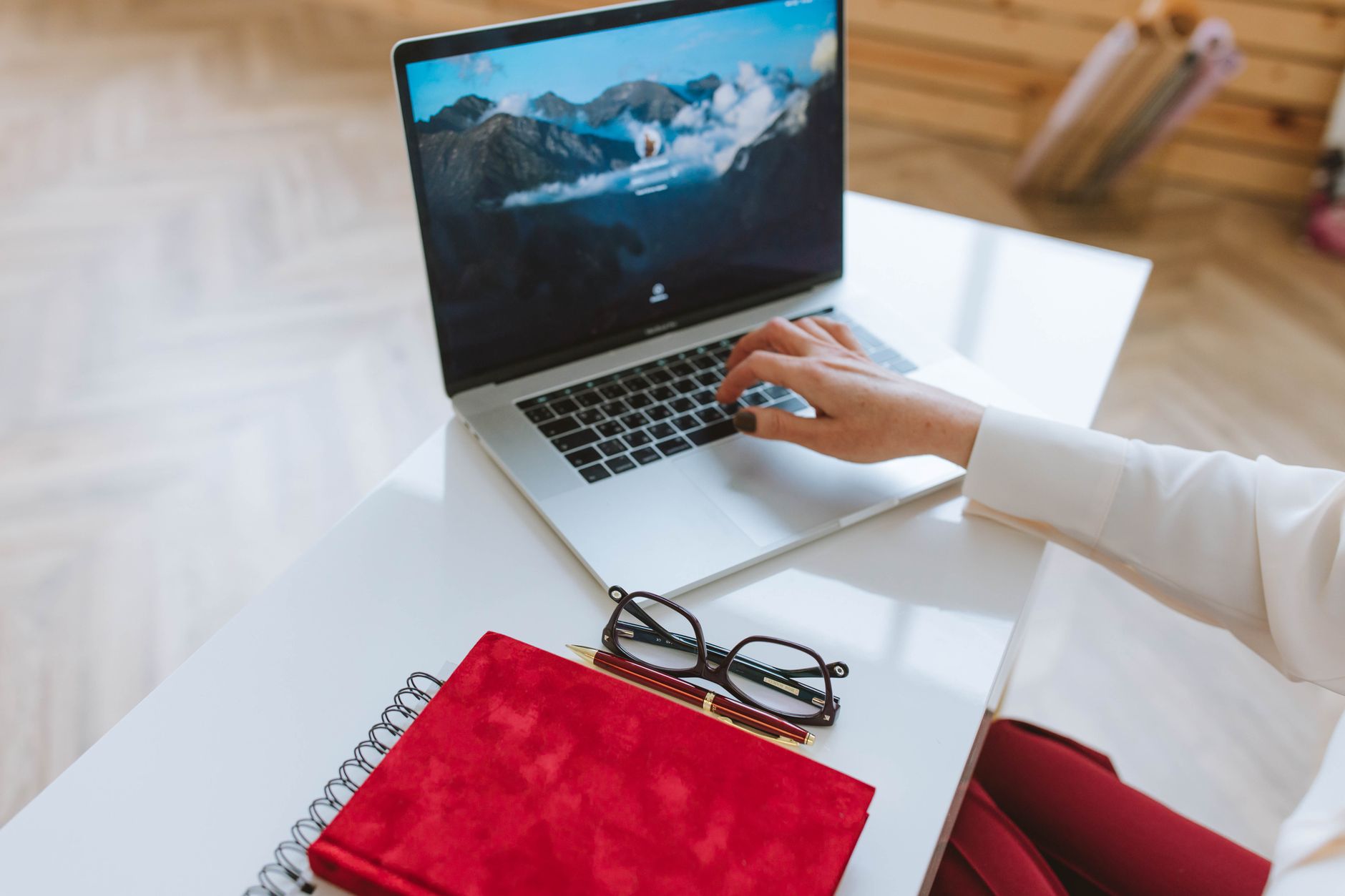 Entrepreneur working on a laptop beside a notebook and glasses at a clean desk